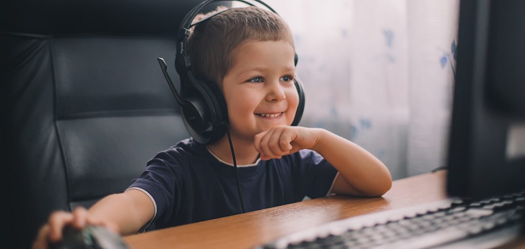 Boy wearing headset at computer, smiling while in an eLuma online therapy session