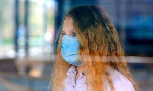 student wearing a mask looking out of a window